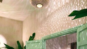 Quarto com cama, mesa de cabeceira, planta em vaso e detalhe decorativo na parede.