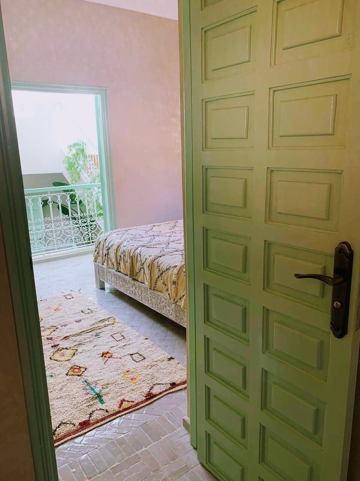 A room with a bed, a patterned rug, and a balcony with a railing.