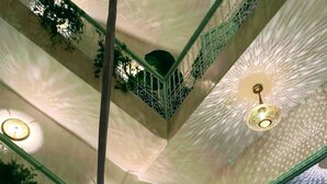 Um interior em vários níveis, com grades decoradas, padrões geométricos no teto e luminárias pendentes.
