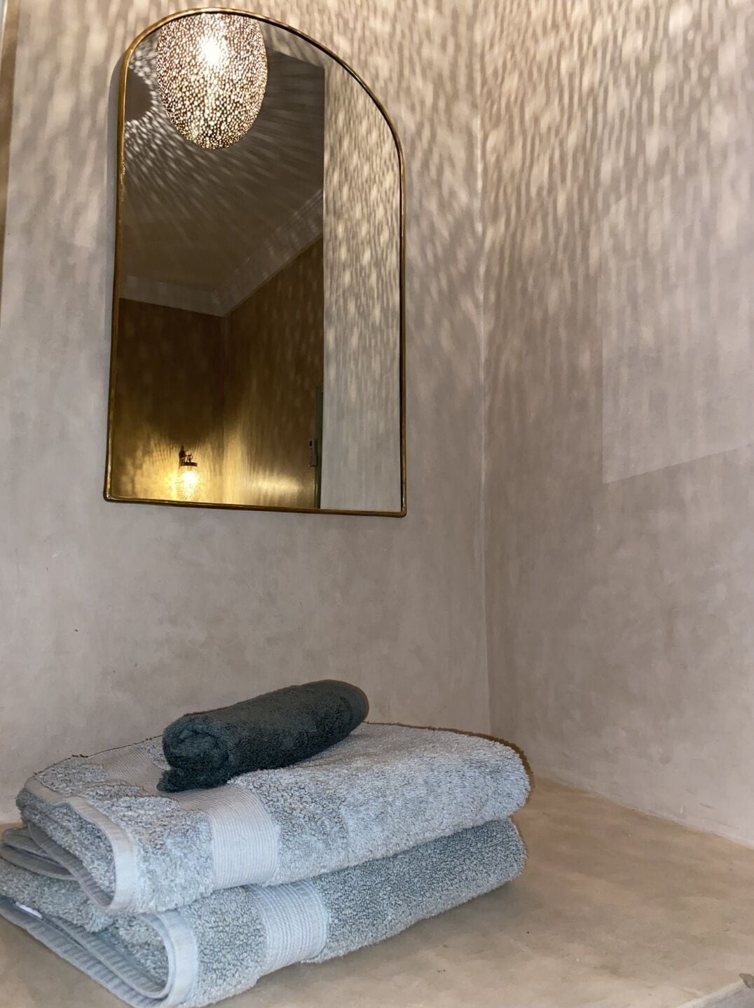 Un baño con una pared con textura, un espejo y una pila de toallas.