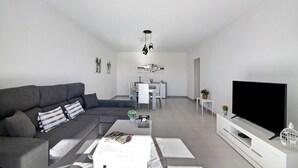 En moderne stue med en grå sofa, et fladskærms-tv og et spisebord i baggrunden.