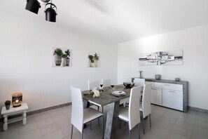 Een eetgedeelte met een tafel gedekt voor twee personen, stoelen, een bank, een wandlamp en een decoratief wandobject.