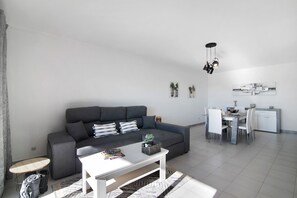 Een moderne woonkamer met een grijze bank, een witte salontafel en een eethoek met een witte tafel en stoelen.