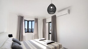 Et moderne soveværelse med seng, gardiner, en hængende lampe og et vindue med udsigt.