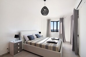 Een slaapkamer met een bed, nachtkastjes, een hanglamp en uitzicht door een raam.