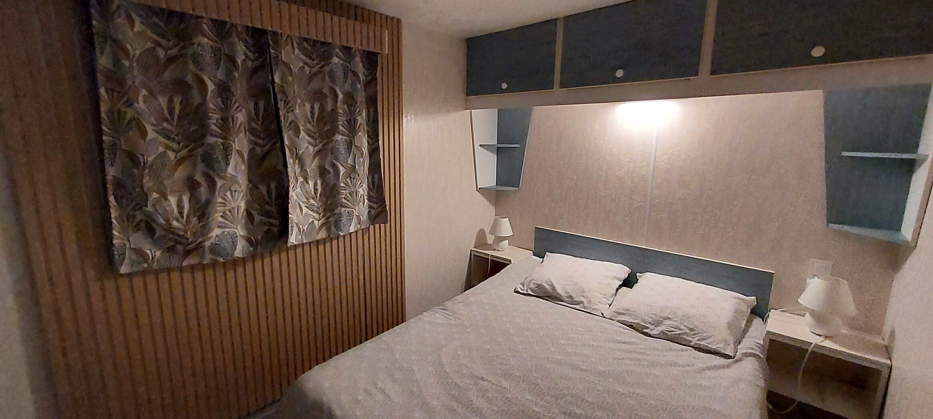 A hotel room with a bed, bedside lamps, a mirror, and a decorative wall panel.