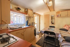 A compact kitchen with a gas stove, wooden cabinets, and a window with curtains.