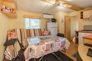 A compact RV interior with a kitchenette, a dining area, and a bed with striped bedding.
