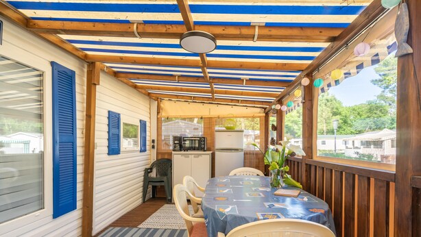 A covered patio with a table and chairs, a kitchen area, and a view of the outside. - Mobile Home 'Mh 100 La Tremblade' with Shared Pool, Terrace, and Private Garden (La Tremblade)