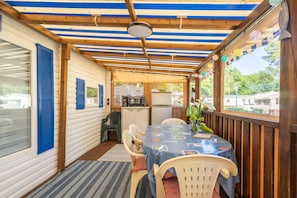 A covered patio with a table and chairs, a kitchen area, and a view of the outside.