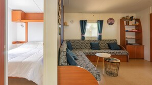 A compact living space with a bed, a sofa, a small table, and a bookshelf. - Mobile Home 'Mh 100 La Tremblade' with Shared Pool, Terrace, and Private Garden (La Tremblade)