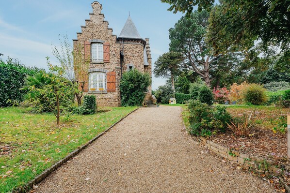 A stone building with a gravel path leading to it, surrounded by greenery.
