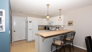 A kitchen with white cabinets, a microwave, a refrigerator, and a bar area with two chairs. - Amazing view from water-front condo! Close to golf courses and great dining. (Camdenton)