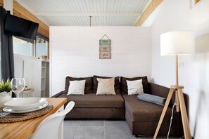 A cozy living area with a brown sofa, a dining table with a white plate and glass, and a floor lamp.