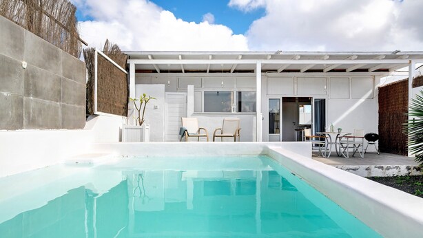 Una piscina con un área de patio techada, una cocina y asientos al aire libre.