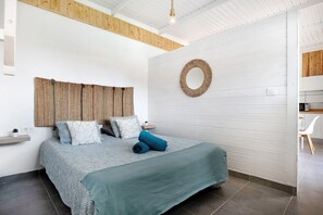 A bedroom with a bed, a wall-mounted mirror, a woven headboard, and a small bedside table.