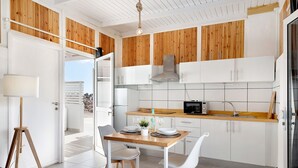Una cocina moderna con armarios blancos, detalles de madera, una mesa de comedor con sillas y vistas a través de una puerta abierta.