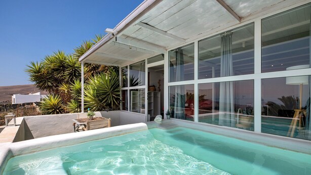 Una piscina con agua cristalina, rodeada de amplias ventanas y plantas.