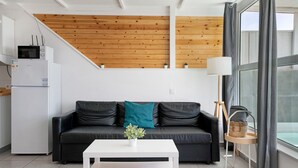Una sala de estar moderna con un sofá de cuero negro, una mesa de centro blanca, techo de madera y un gran ventanal con cortinas.