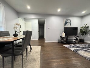 A modern living room with a dining area, a flat-screen TV, and a potted plant. - "Tranquil Getaway: Stay Serenity in Suburban Bliss!" (Hempstead)