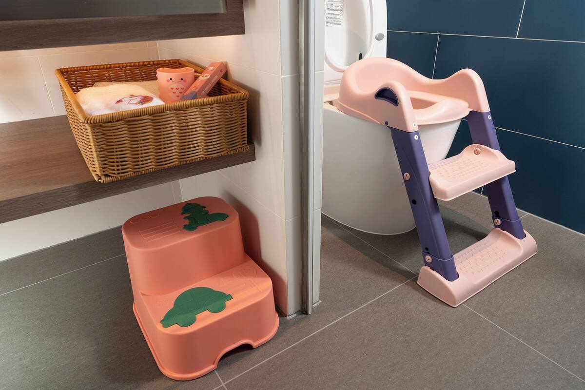 A bathroom with a wicker basket shelf, a pink and green step stool, and a pink potty chair.