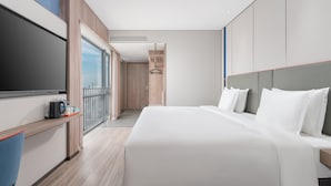 Una habitación de hotel moderna con una cama grande, televisión, escritorio con silla y balcón con vistas.