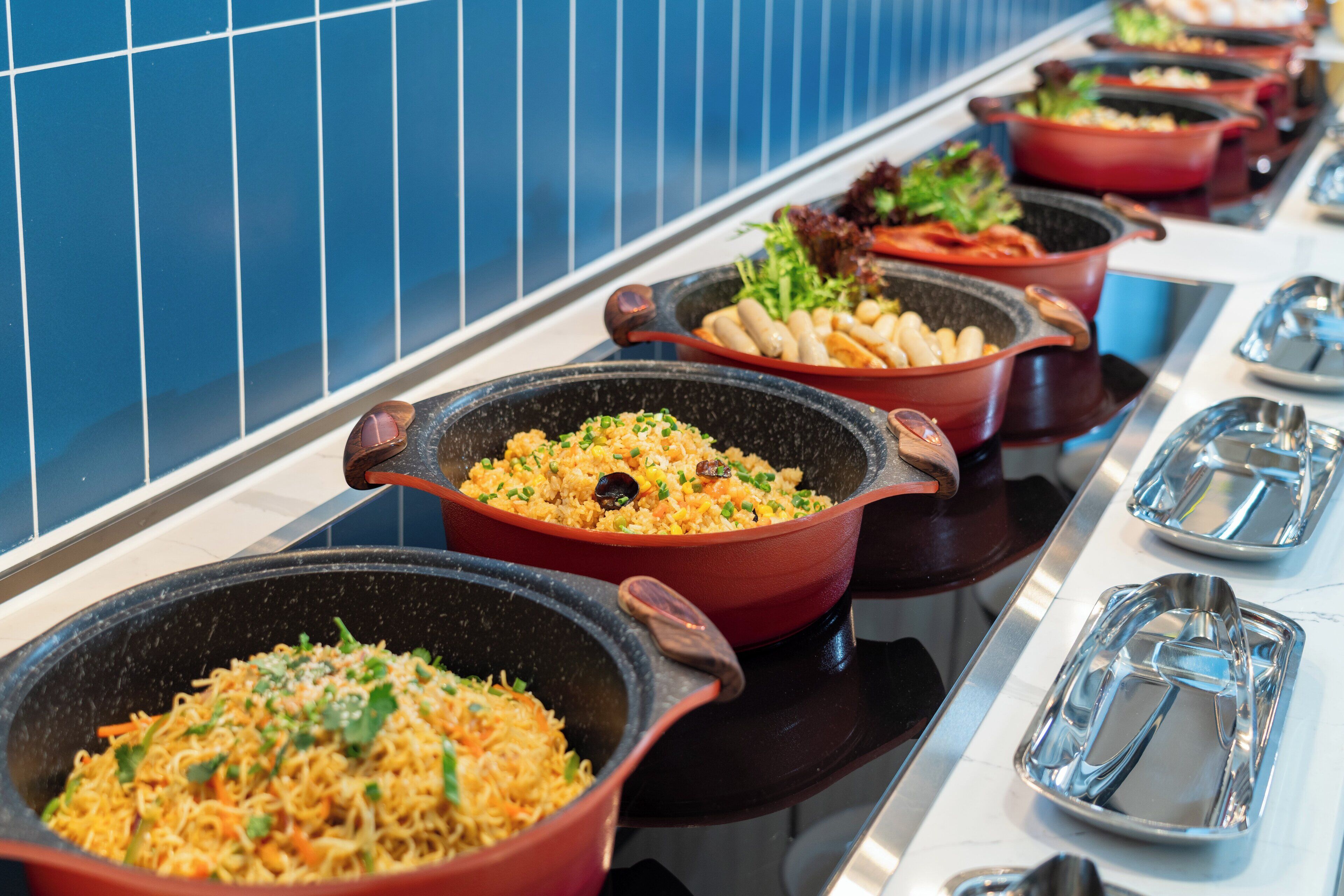 A buffet with various dishes in large pots, including noodles and vegetables.