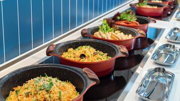 Un buffet proposant divers plats servis dans de grands récipients, notamment des nouilles et des légumes.