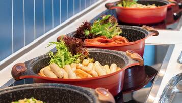 Een buffet met diverse gerechten in grote pannen, waaronder salades, vlees en rijst.