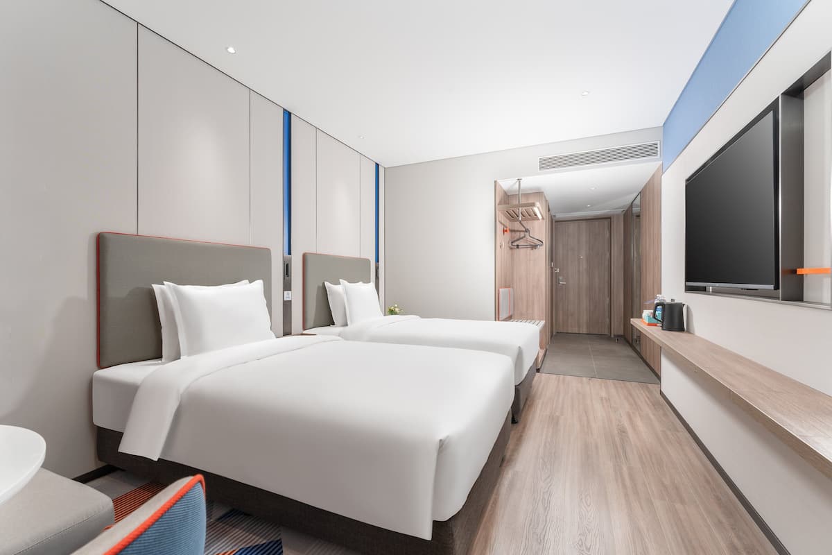 A modern hotel room with two beds, a desk, and a large TV.