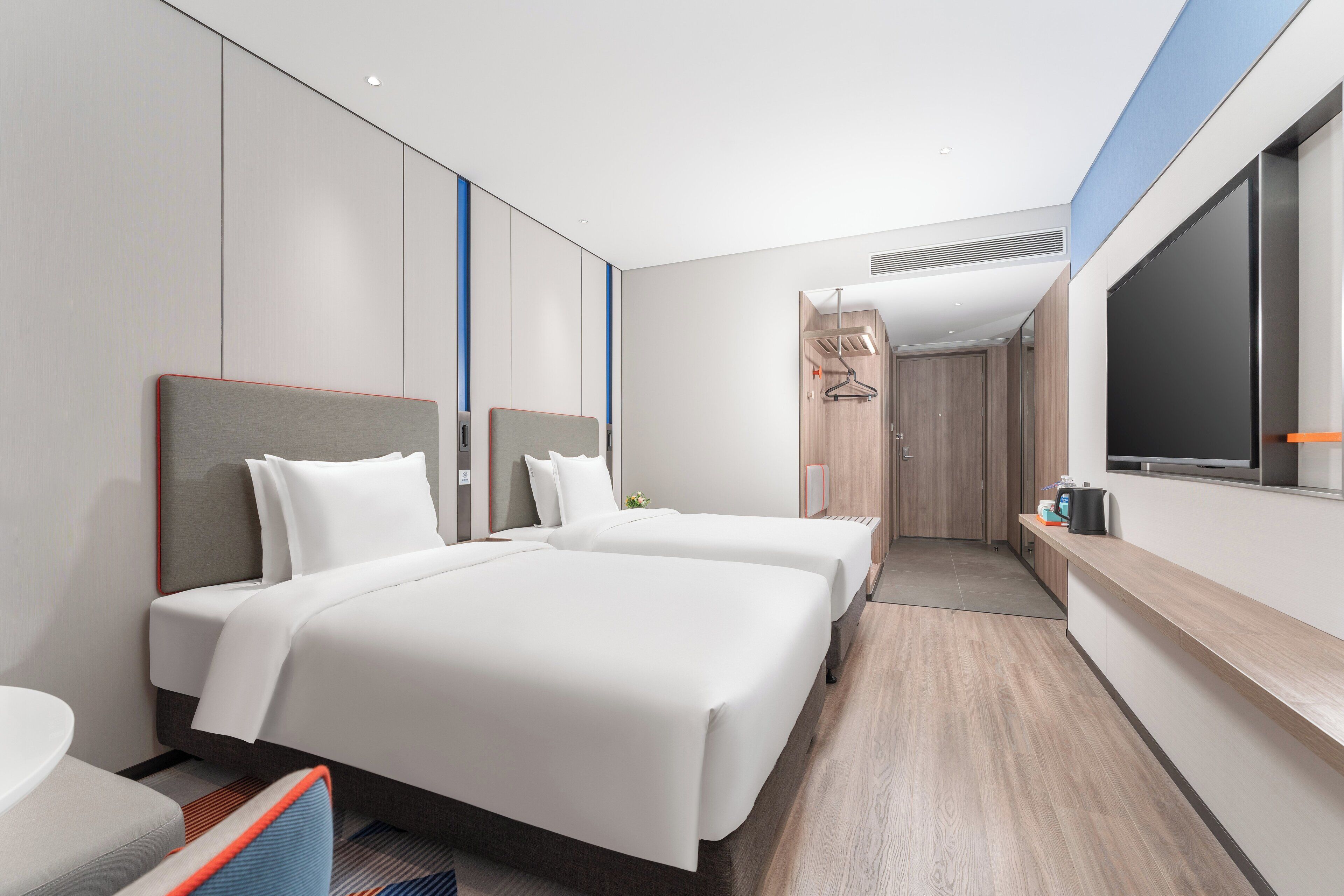 A modern hotel room with two beds, a large window, and a flat-screen TV.