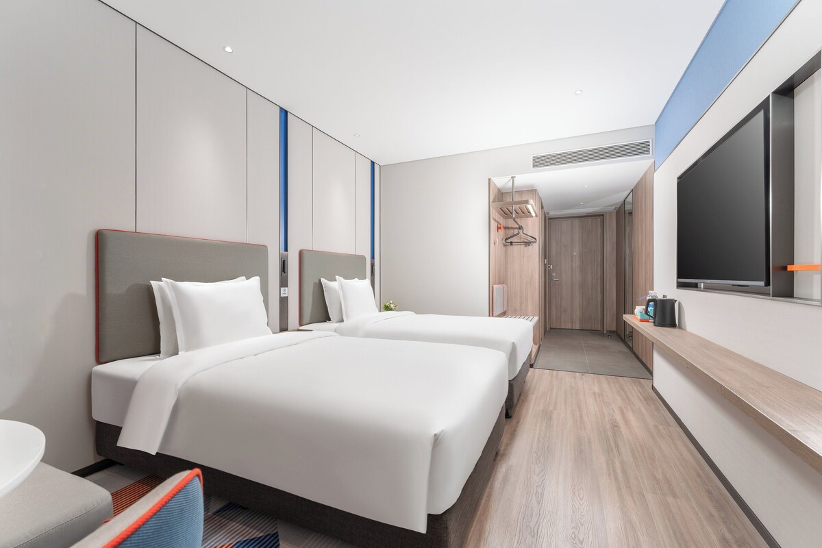 A modern hotel room with two beds, a desk, and a large TV.