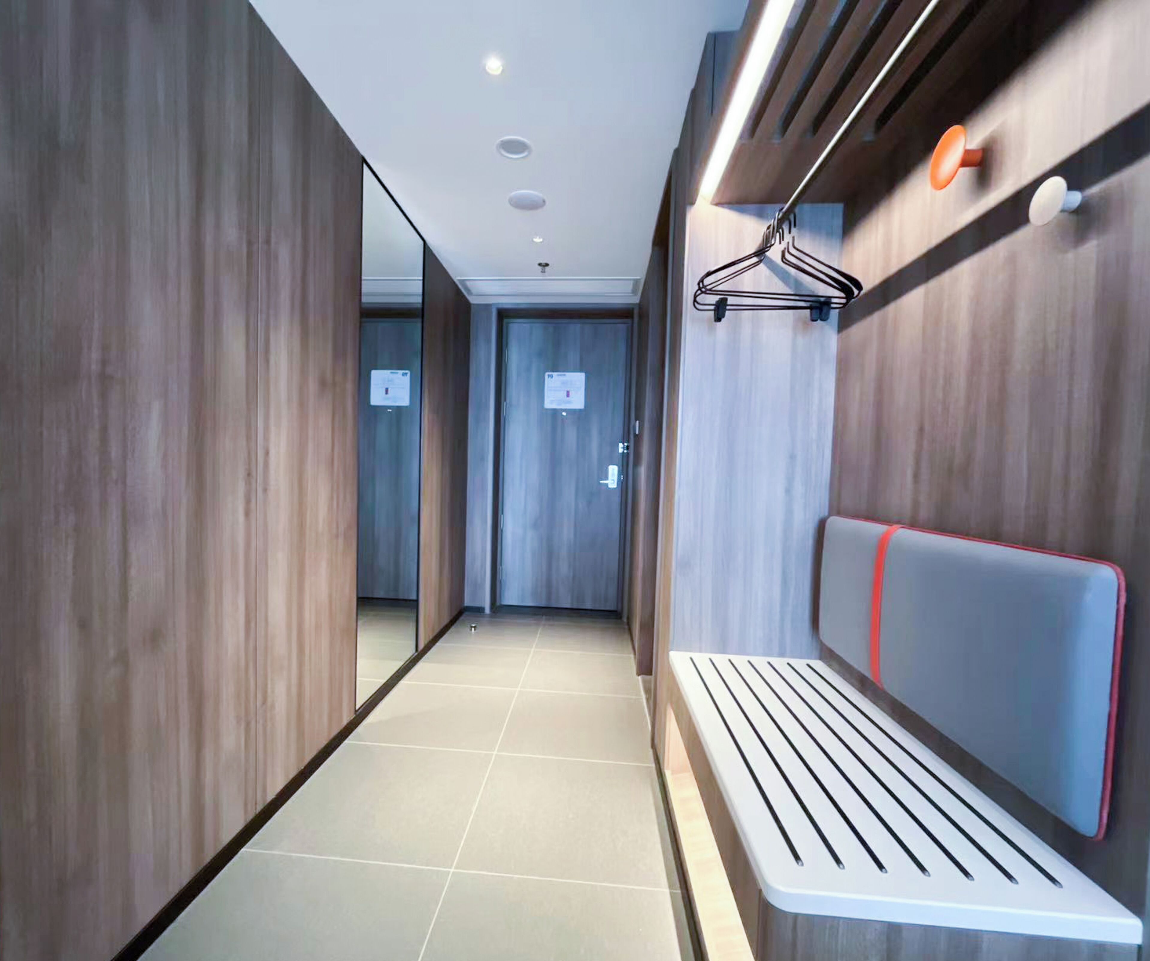 A modern hallway with wooden walls, a bench with a red stripe, and a coat hanger on the wall.
