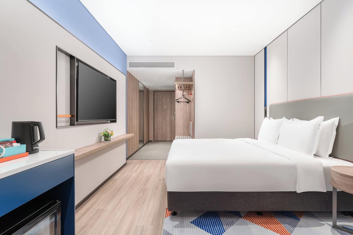 A modern hotel room with a large bed, a flat-screen TV, a desk with a coffee maker, and a walk-in closet.