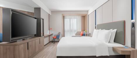 Una habitación de hotel moderna con una gran televisión de pantalla plana, una cama con ropa blanca, un escritorio con una silla y una ventana con cortinas traslúcidas.