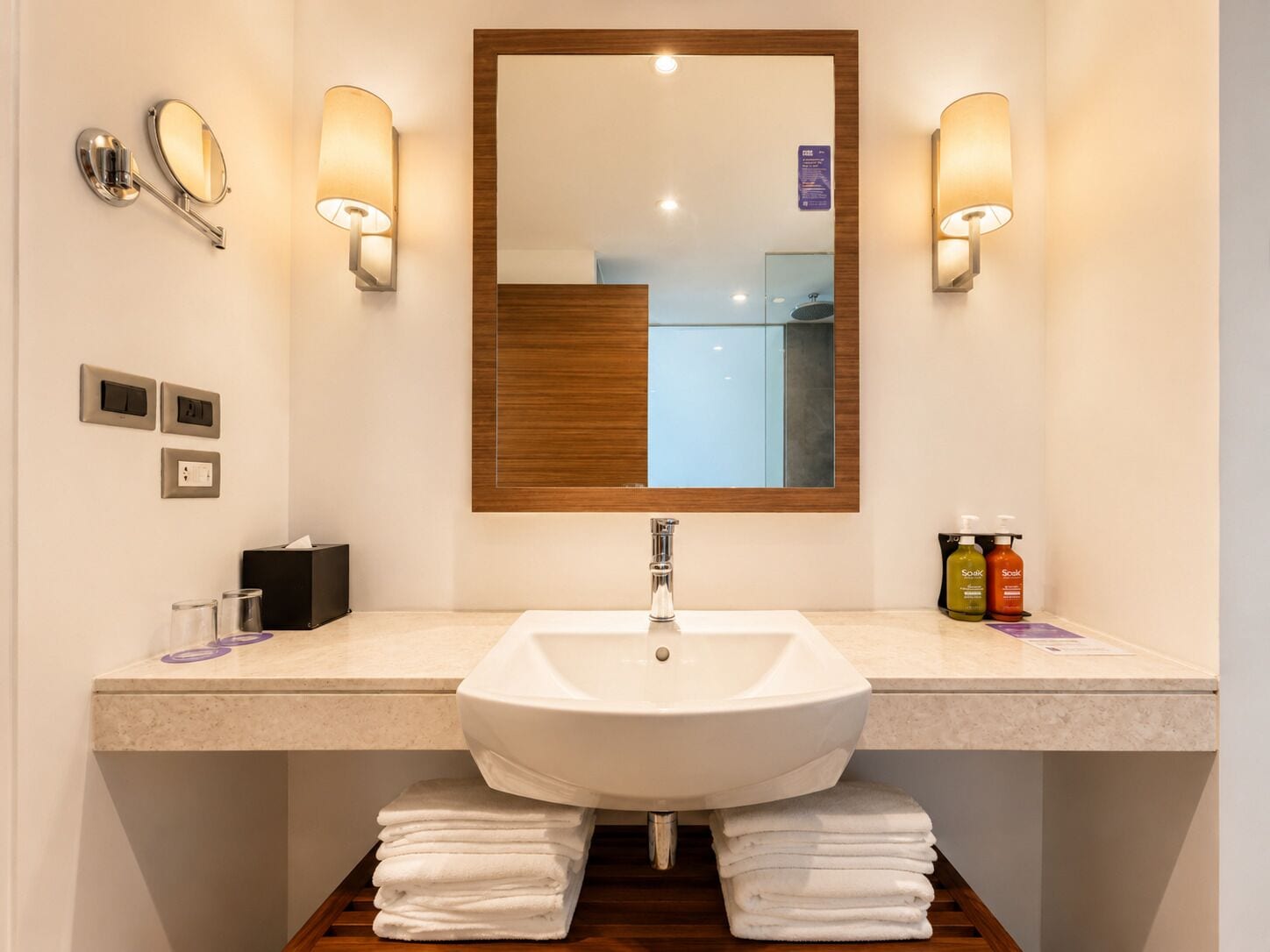 A bathroom with a white sink, wooden vanity, two wall-mounted mirrors, and a large mirror above the sink.
