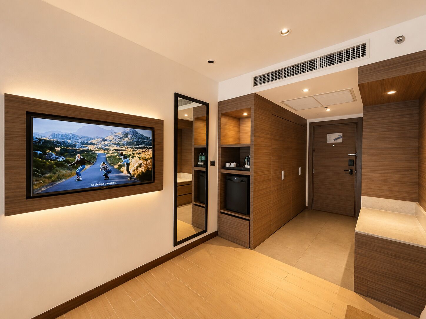 Une chambre d’hôtel moderne dotée d’un grand téléviseur à écran plat fixé au mur, d’une armoire intégrée et d’un miroir.