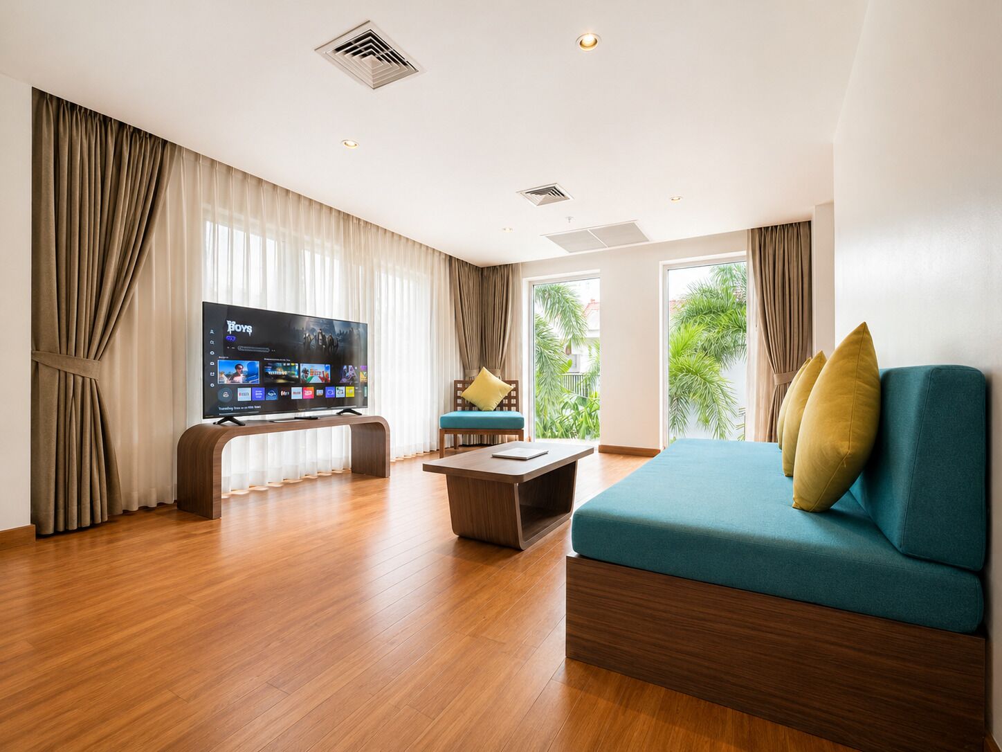 Ein modernes Wohnzimmer mit Flachbildfernseher, einer Couch, einem Couchtisch und Blick auf Grünflächen.