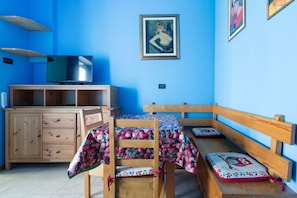 A room with a blue wall, a wooden cabinet, a television, a wooden bench, and a table with a floral tablecloth.