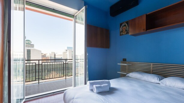 Een hotelkamer met een bed, een raam met uitzicht op de stad, een houten hoofdeinde en een wandplank.