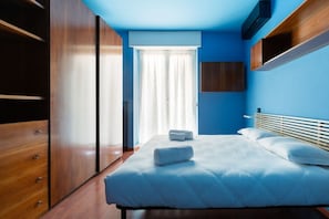 Une chambre à coucher comprenant un lit, une armoire, une fenêtre avec des rideaux et un téléviseur fixé au mur.