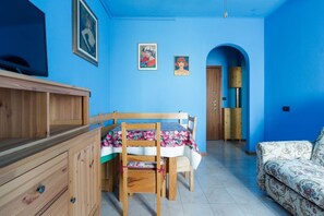 A room with a blue wall, a wooden cabinet, a table with chairs, a sofa, and a door leading to another room.