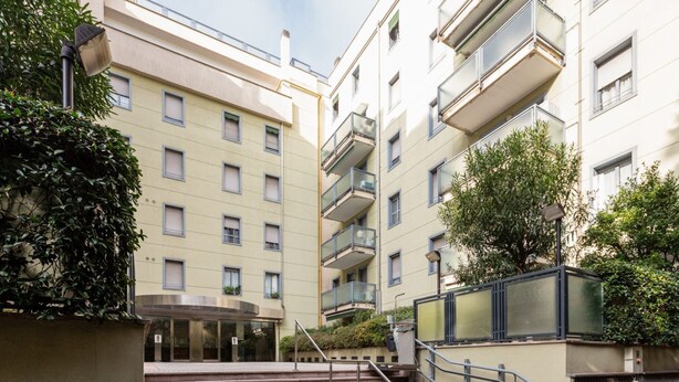 A multi-story building with a central staircase, balconies, and greenery.