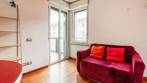 A room with a red sofa, a wooden floor, a glass door leading outside, and a small window.
