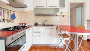 A compact kitchen with a gas stove, white cabinets, a red countertop, and a small bar stool.