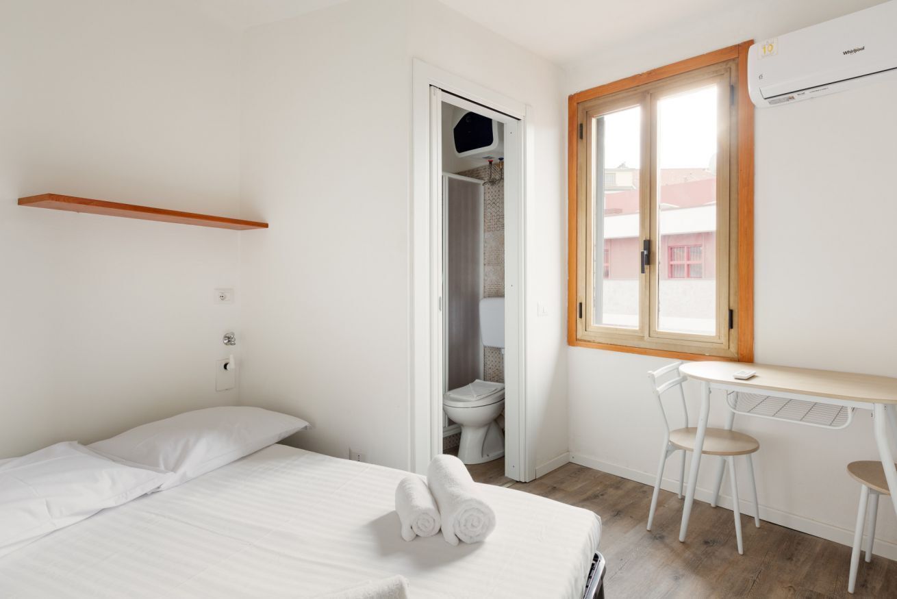 A room with a bed, a small table with chairs, a window, and a door leading to a bathroom.
