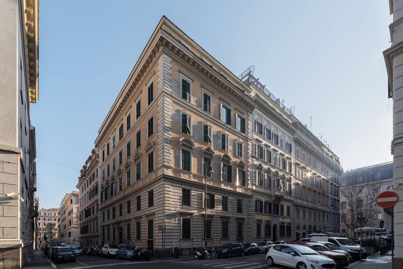 Un immeuble à plusieurs étages, doté d’une architecture classique, qui se distingue par son entrée d’angle imposante, ses nombreuses fenêtres et sa façade visible depuis la rue.