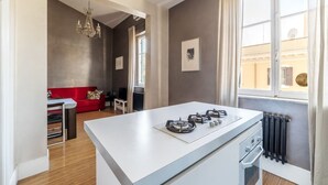Et moderne køkken med en central ø, et spiseområde med en rød sofa og en lysekrone.