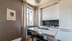 Et moderne køkken med en central ø, barstole og et stort vindue med gardiner.