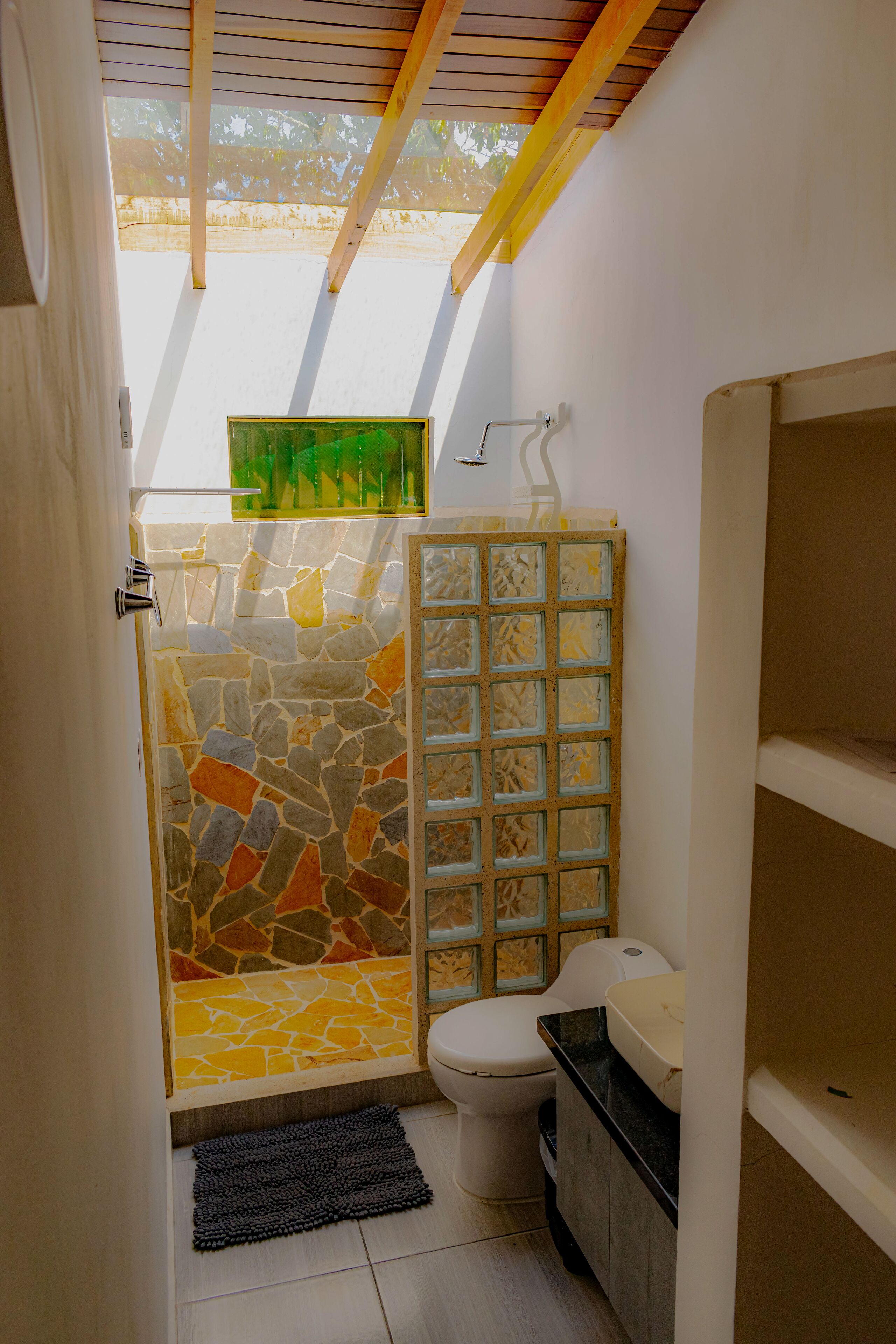 Een kleine badkamer met een douchecabine van natuursteen, een toilet en een wastafel.